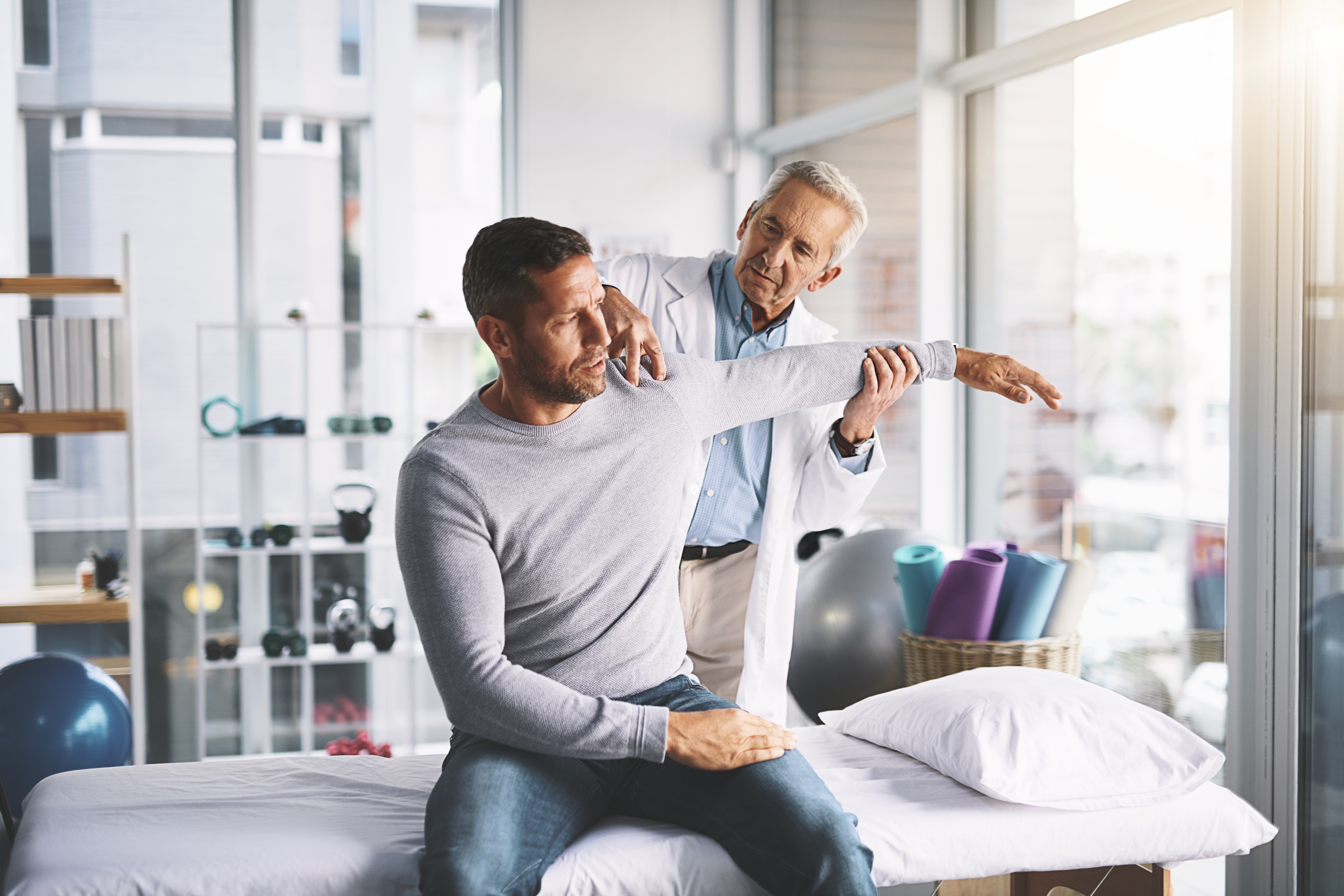 An orthopedic doctor helps guide a patient shoulder in an exam for shoulder impingement.