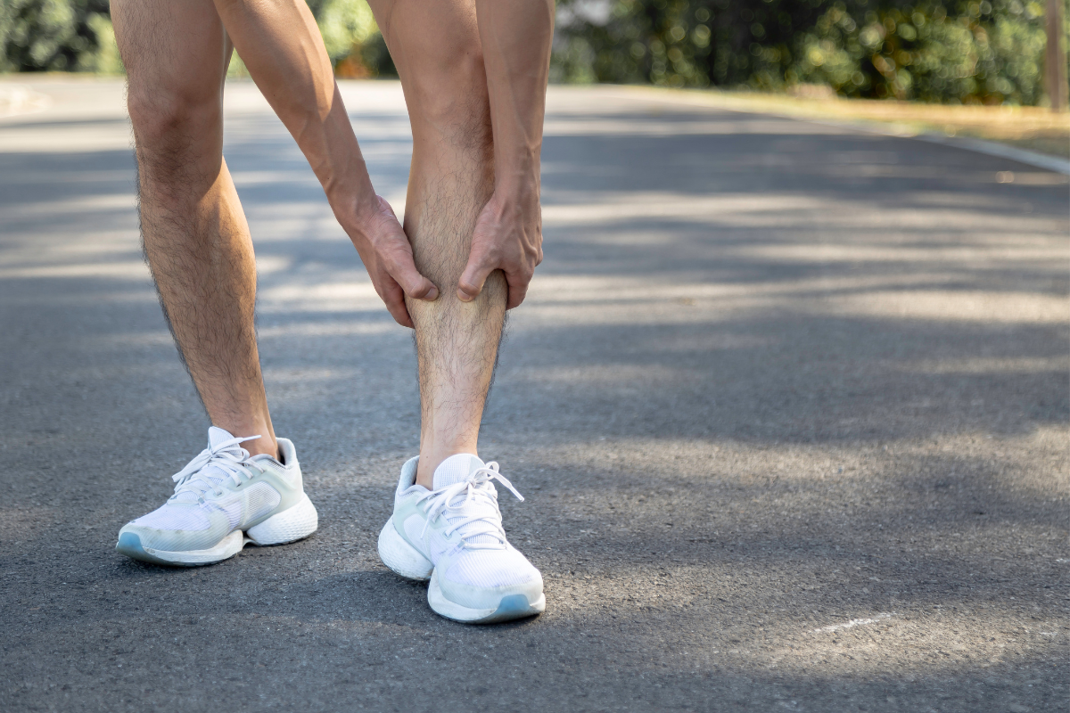 A runner pauses on a pavement path holding their shin as a result of pain.