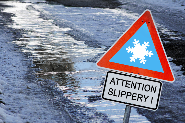 Black ice on a sidewalk with a caution sign stating attention slippery!